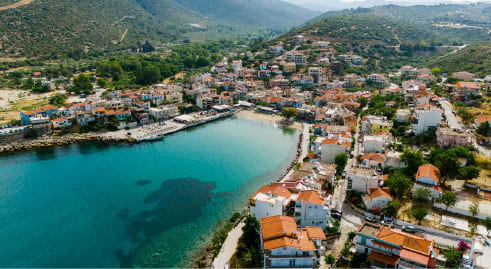 Aerial view of a colourful Thassos waterfront village with orange rooftops and turquoise bay